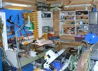 Et verkstedrom med arbeidsbenk, verktøy, lamper og hyller fulle av utstyr.